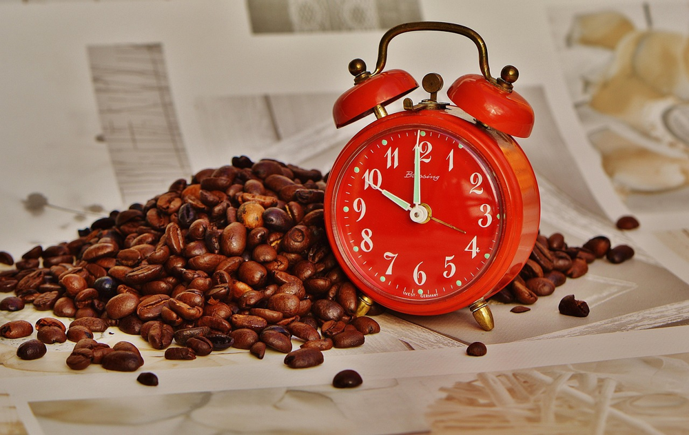 A classic alarm clock surrounded by coffee beans, symbolizing the link between our sleep–wake schedule and meal times. Aligning meals with wake hours (and fasting overnight) has been shown to lower inflammation and improve metabolic markers.